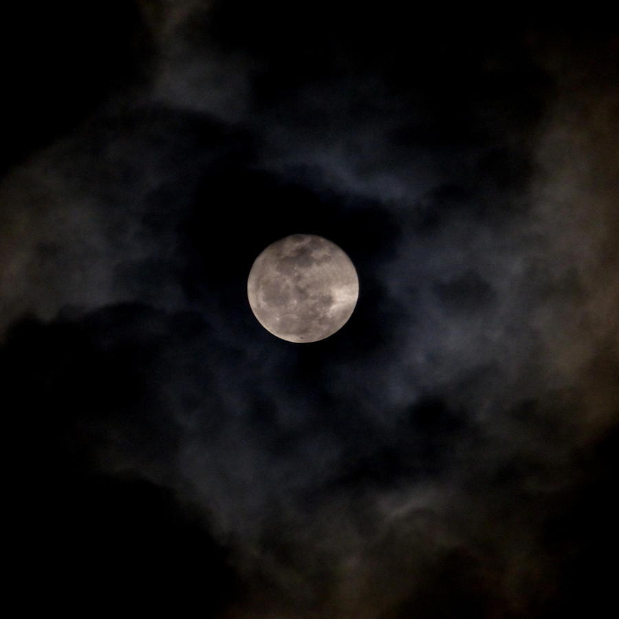 a light of full moon peaks through the clouds